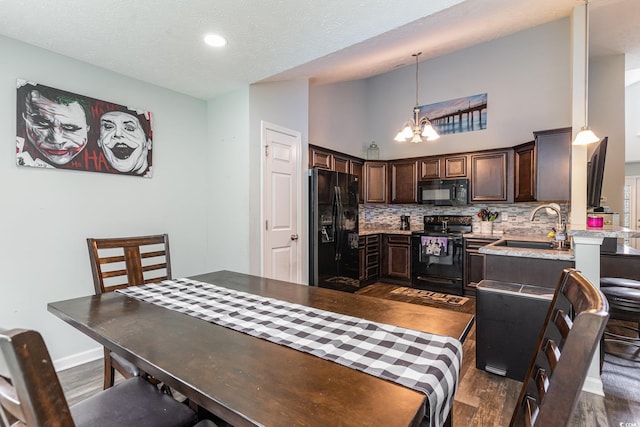 kitchen with hanging light fixtures, tasteful backsplash, a towering ceiling, dark brown cabinets, and black appliances