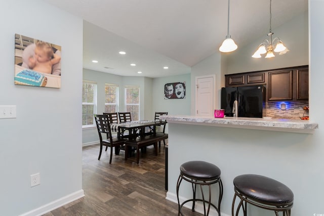 kitchen with dark brown cabinetry, hanging light fixtures, a kitchen breakfast bar, tasteful backsplash, and black fridge