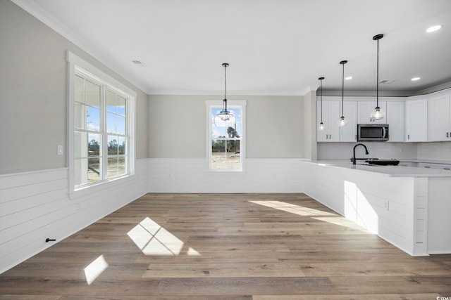 unfurnished dining area with sink, light wood-type flooring, and ornamental molding