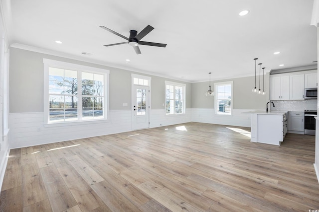 unfurnished living room featuring sink, ceiling fan, light hardwood / wood-style floors, and crown molding