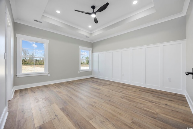 empty room with ornamental molding, light hardwood / wood-style flooring, plenty of natural light, and a tray ceiling