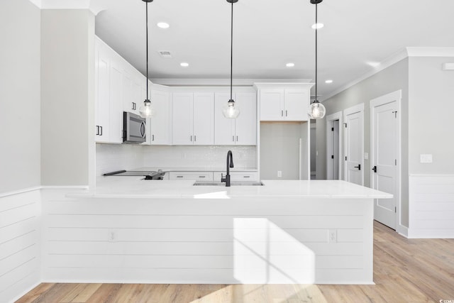 kitchen featuring kitchen peninsula, pendant lighting, crown molding, white cabinetry, and sink