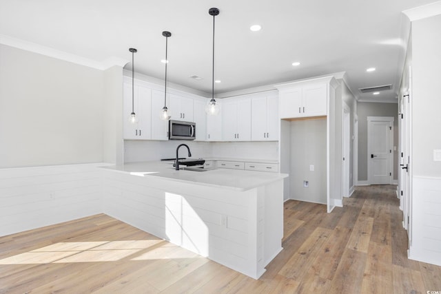 kitchen featuring hanging light fixtures, light wood-type flooring, kitchen peninsula, ornamental molding, and white cabinets