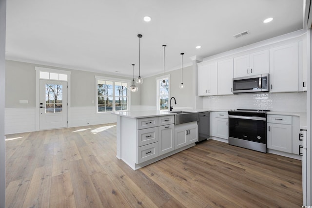 kitchen featuring appliances with stainless steel finishes, crown molding, kitchen peninsula, pendant lighting, and white cabinetry