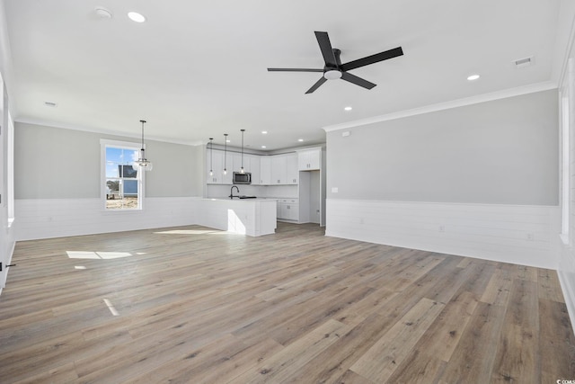 unfurnished living room with ceiling fan with notable chandelier, light hardwood / wood-style floors, crown molding, and sink