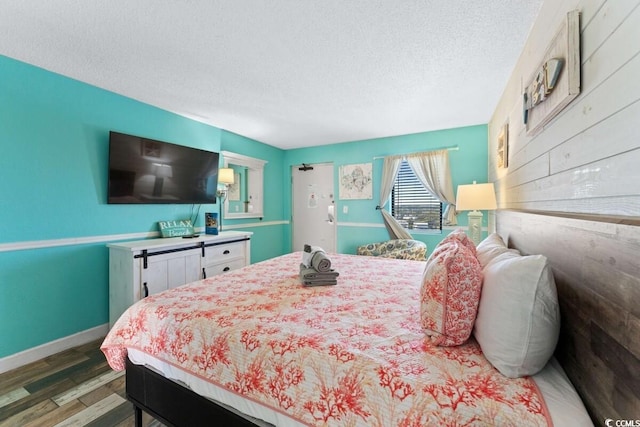 bedroom featuring a textured ceiling, hardwood / wood-style flooring, and wood walls