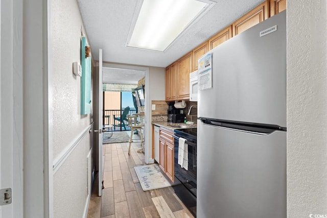 kitchen with black / electric stove, light hardwood / wood-style flooring, tasteful backsplash, light stone counters, and stainless steel refrigerator