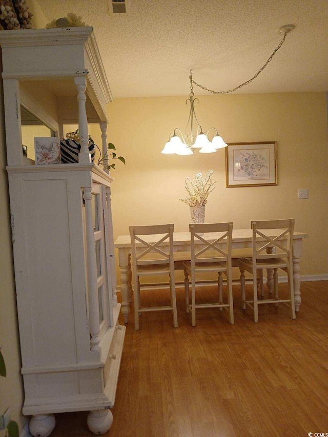 dining area with hardwood / wood-style floors, a textured ceiling, and a notable chandelier