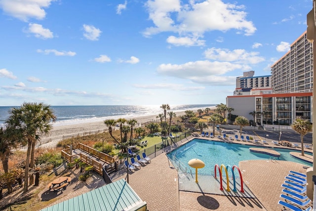 view of swimming pool featuring a patio area, a water view, and a beach view