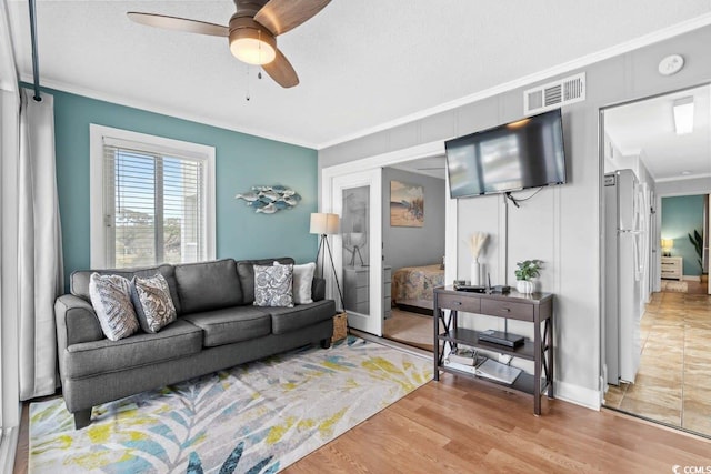 living room with hardwood / wood-style flooring, ceiling fan, a textured ceiling, and ornamental molding