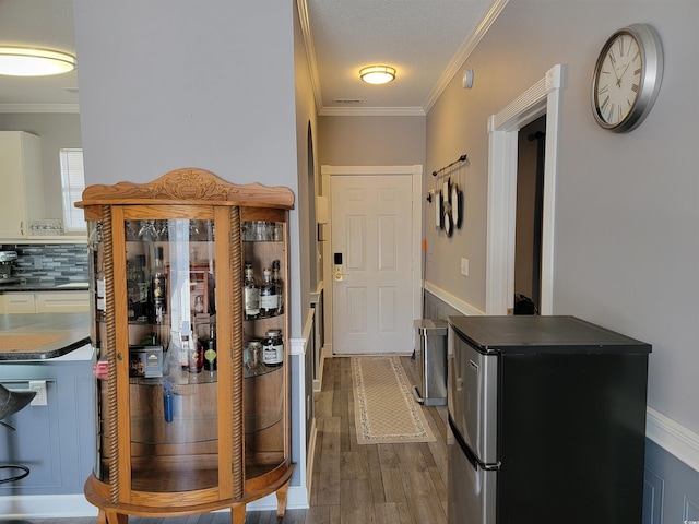 interior space with a textured ceiling, hardwood / wood-style flooring, stainless steel refrigerator, and crown molding