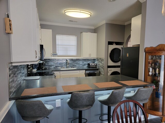 kitchen with kitchen peninsula, a kitchen breakfast bar, stacked washer and dryer, and white cabinetry