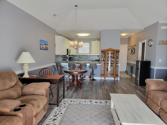 living room featuring hardwood / wood-style flooring, lofted ceiling, crown molding, and an inviting chandelier