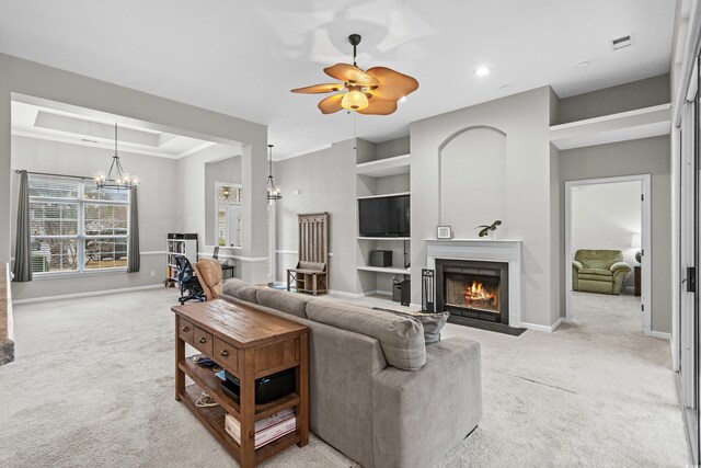 carpeted living room featuring ceiling fan with notable chandelier and built in shelves