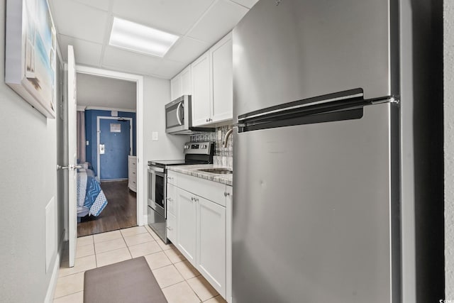 kitchen with white cabinetry, light tile patterned floors, stainless steel appliances, and light stone counters