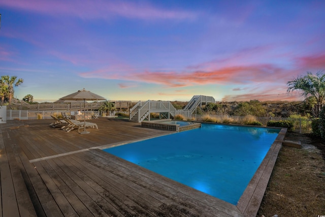 pool at dusk with a wooden deck and an in ground hot tub