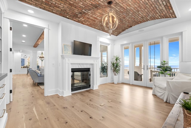 living room featuring french doors, light hardwood / wood-style flooring, vaulted ceiling, brick ceiling, and a fireplace