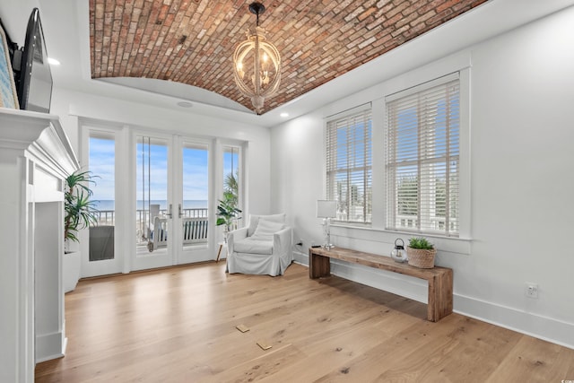 sitting room with french doors, an inviting chandelier, lofted ceiling, brick ceiling, and a water view