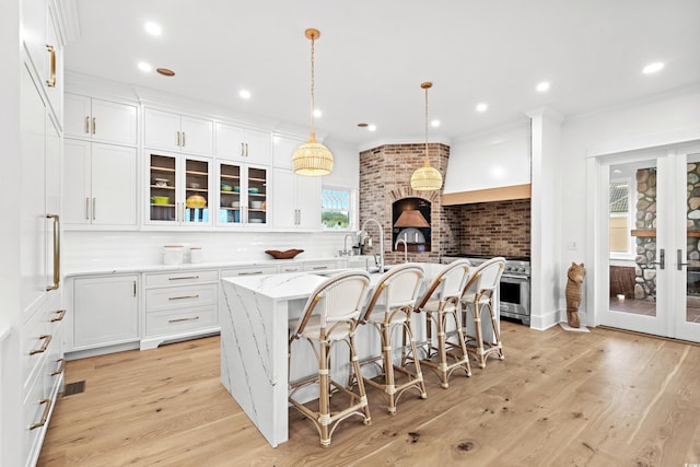 kitchen featuring backsplash, white cabinets, an island with sink, decorative light fixtures, and light stone counters