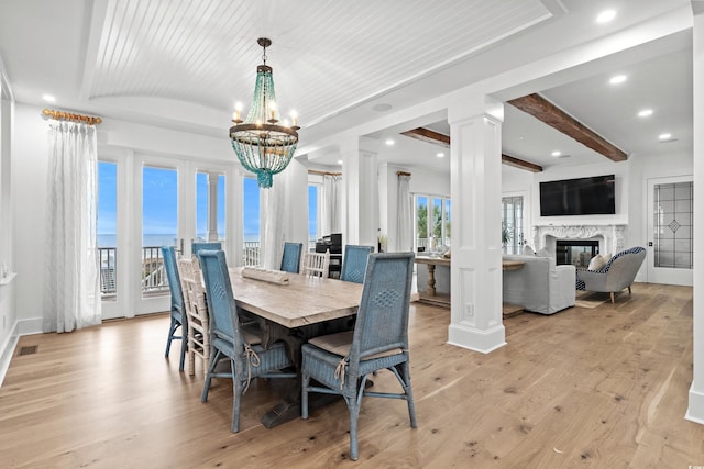 dining area featuring light hardwood / wood-style flooring, ornate columns, a premium fireplace, beamed ceiling, and a notable chandelier