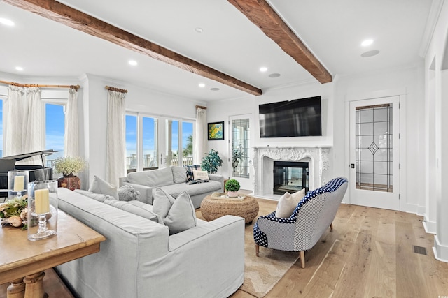 living room featuring beamed ceiling, light wood-type flooring, ornamental molding, and a high end fireplace