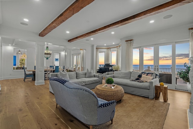 living room featuring beam ceiling, a water view, a notable chandelier, and light wood-type flooring