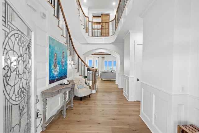 foyer entrance with a towering ceiling, light hardwood / wood-style flooring, and crown molding