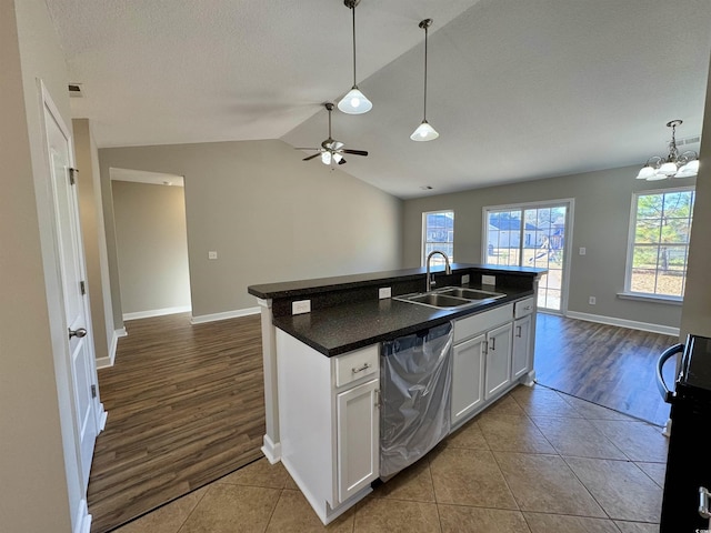 kitchen featuring dishwasher, white cabinetry, an island with sink, vaulted ceiling, and light tile patterned floors