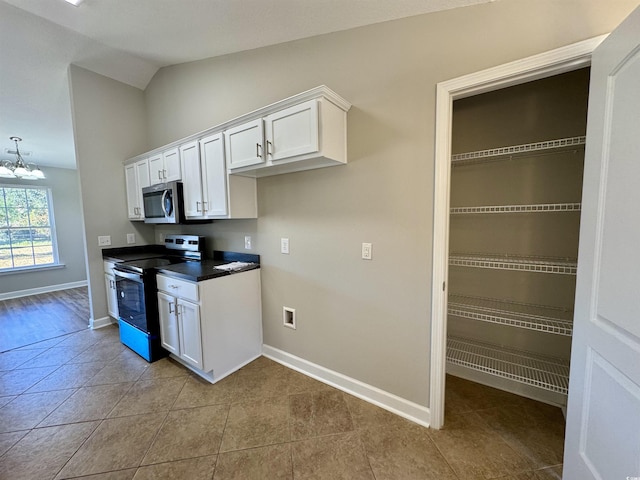 kitchen featuring lofted ceiling, white cabinetry, stainless steel appliances, light tile patterned floors, and a chandelier