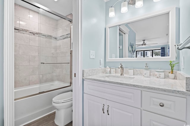 full bathroom featuring toilet, enclosed tub / shower combo, ceiling fan, wood-type flooring, and vanity