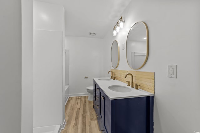 full bath featuring double vanity, wood finished floors, a sink, and toilet