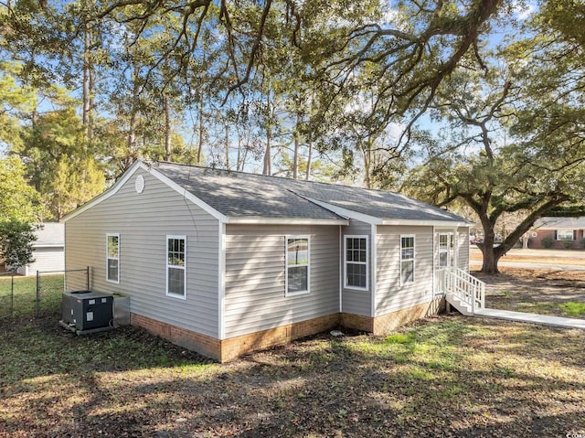 view of home's exterior featuring fence, cooling unit, and roof with shingles