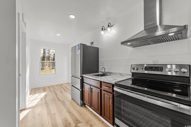 kitchen featuring range hood, light wood finished floors, appliances with stainless steel finishes, a sink, and light stone countertops