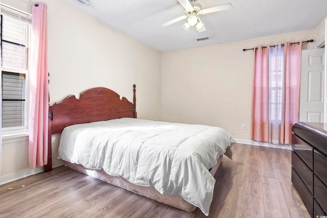 bedroom featuring ceiling fan, wood-type flooring, and a textured ceiling