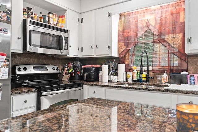 kitchen featuring decorative backsplash, stainless steel appliances, sink, dark stone countertops, and white cabinetry