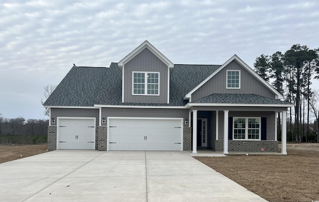 craftsman-style home featuring a shingled roof, brick siding, driveway, and a porch