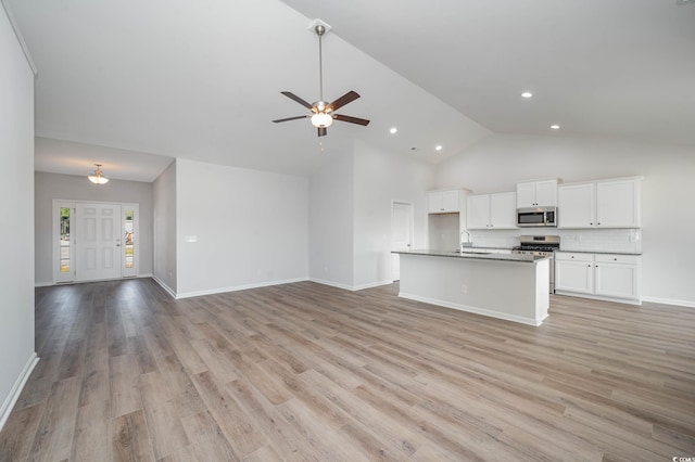 kitchen featuring high vaulted ceiling, backsplash, light hardwood / wood-style floors, a kitchen island with sink, and white cabinets