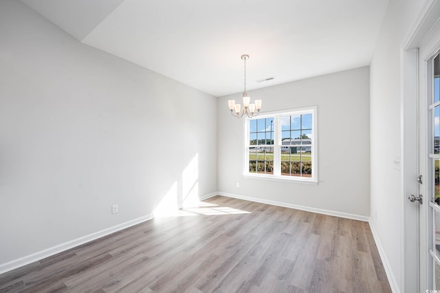 spare room featuring a chandelier and light wood-type flooring