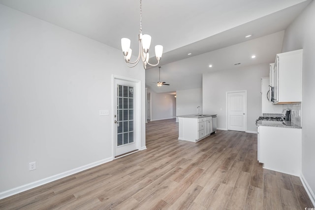 interior space featuring white cabinets, ceiling fan with notable chandelier, hanging light fixtures, and a kitchen island with sink