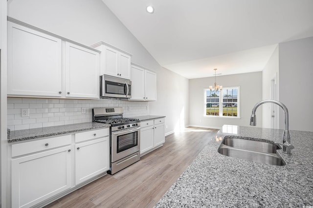 kitchen with stone counters, white cabinetry, sink, stainless steel appliances, and lofted ceiling