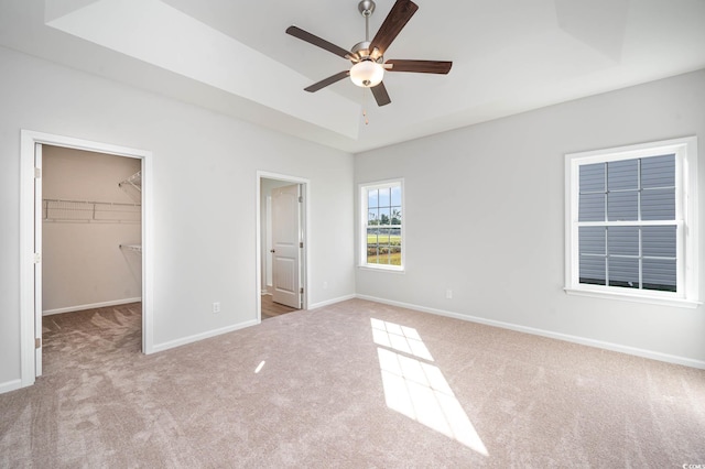 unfurnished bedroom featuring a tray ceiling, light colored carpet, ceiling fan, a spacious closet, and a closet