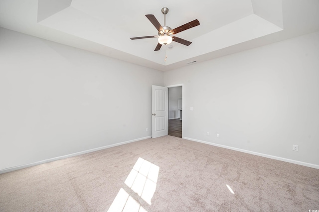 carpeted spare room with a tray ceiling and ceiling fan