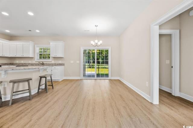 kitchen with a breakfast bar area, light stone counters, decorative light fixtures, light hardwood / wood-style flooring, and white cabinets