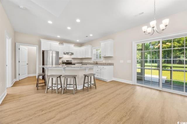 kitchen featuring a kitchen bar, decorative light fixtures, a center island, stainless steel refrigerator, and white cabinets