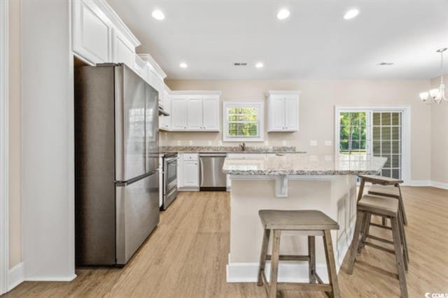 kitchen featuring a kitchen island, white cabinetry, hanging light fixtures, light hardwood / wood-style floors, and stainless steel appliances