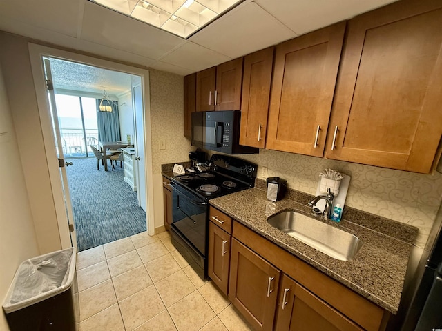 kitchen featuring sink, a drop ceiling, dark stone counters, light tile patterned flooring, and black appliances