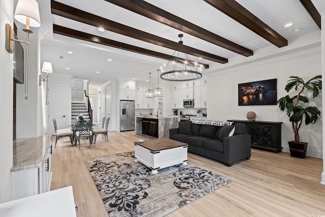 living room featuring sink, beamed ceiling, a notable chandelier, crown molding, and light hardwood / wood-style floors