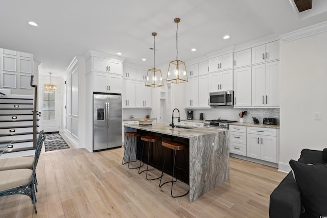 kitchen featuring white cabinetry, sink, hanging light fixtures, a kitchen island with sink, and appliances with stainless steel finishes