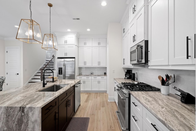 kitchen featuring appliances with stainless steel finishes, light stone counters, sink, white cabinets, and hanging light fixtures