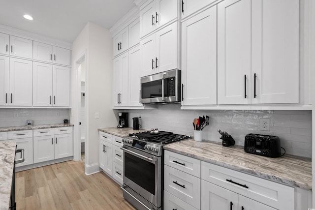 kitchen with appliances with stainless steel finishes, tasteful backsplash, light hardwood / wood-style floors, light stone counters, and white cabinetry